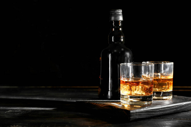 暗い木製の背景に冷たいウイスキーのボトルとグラス - 写真・画像