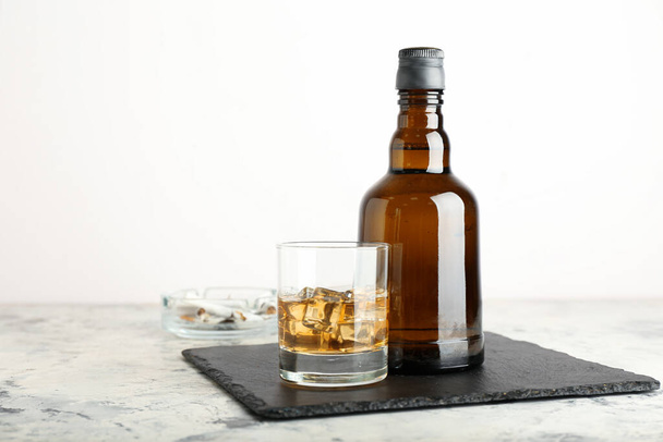 Μπουκάλι και ποτήρι κρύο ουίσκι σε ελαφρύ φόντο - Φωτογραφία, εικόνα