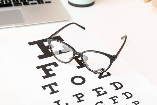 Stijlvolle bril met oogtestkaart op tafel, close-up - Foto, afbeelding
