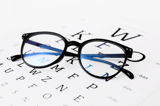 Stilvolle Brille mit Sehtest-Diagramm auf weißem Hintergrund, Nahaufnahme - Foto, Bild
