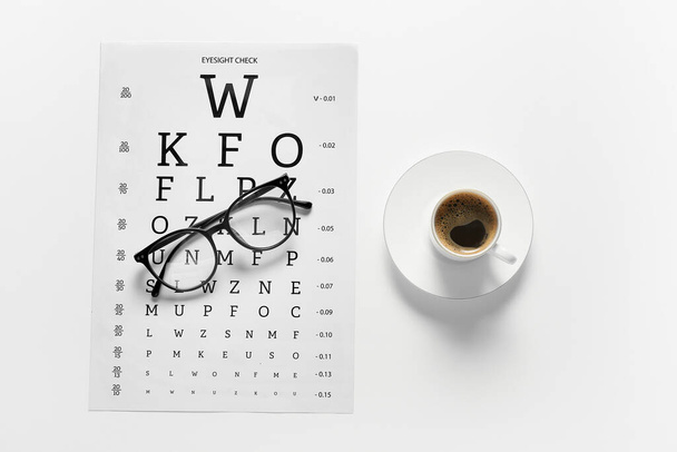 Eyeglasses with eye test chart and cup of coffee on white background - Photo, Image