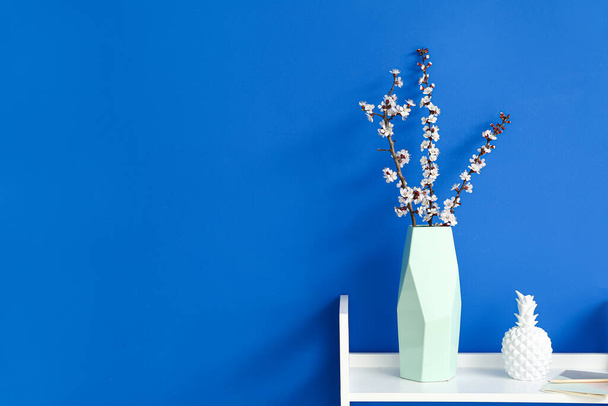Vase with blooming spring branches on table near color wall - Foto, immagini