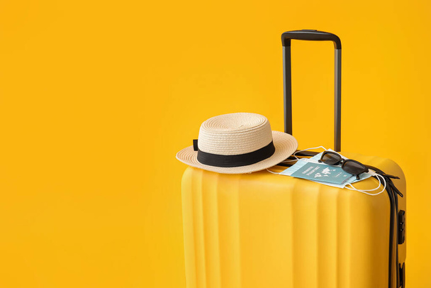 Packed suitcase with immune passport, medical masks, hat and sunglasses on color background - Photo, Image
