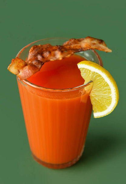 Glass of bloody mary cocktail garnished with bacon and lemon on color background - Photo, Image