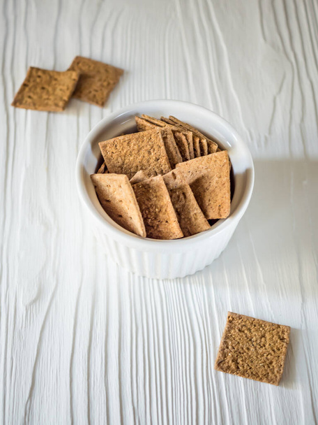 Natural flat mini breads of a square shape in a white bowl on a wooden light background. Delicious and quick snack for diet food - Foto, imagen