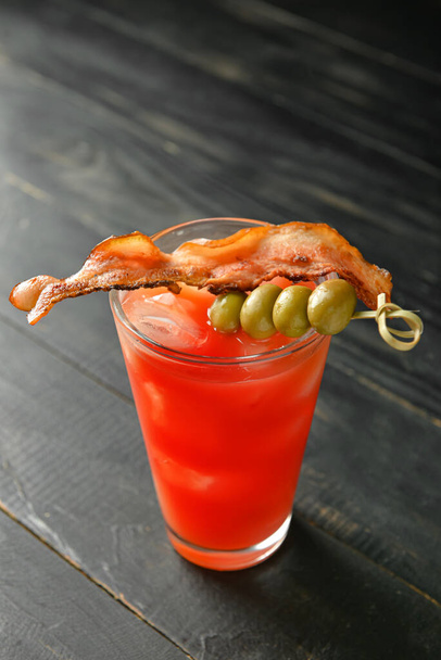 Glass of bloody mary cocktail garnished with bacon and olives on dark wooden background - Photo, Image