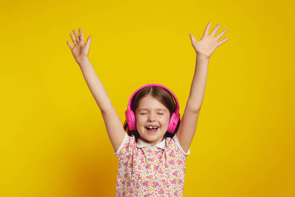 Girl dancing in wireless headphones with closed eyes, keeps hands raised - Foto, Imagen
