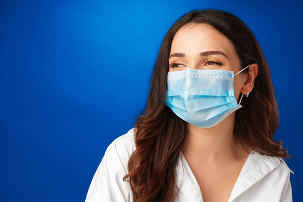 Young beautiful brunette woman wearing medical face mask against blue background - Foto, Imagem