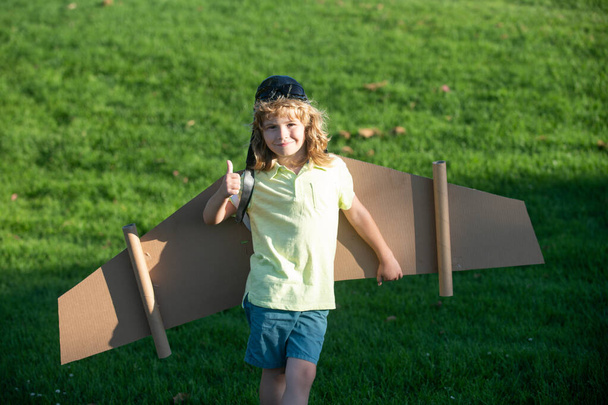 Kids fly. Funny child boy with thumbs up smile wear pilot hat and goggles flying with toy cardboard airplane wings, Start up freedom concept, carefree kid. - Foto, imagen