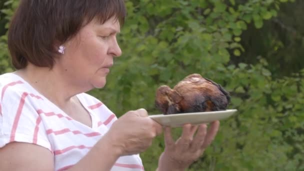 Hermosa foto de una señora de mediana edad oliendo un pollo a la parrilla. - Metraje, vídeo
