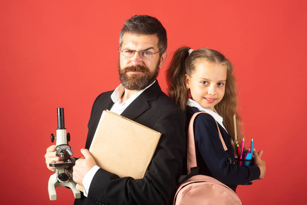 Elementary pupil with teacher in red studio, isolated. Portrait of funny school girl and tutor with school supplies. Happy teacher and student girl on red. - Foto, Imagem