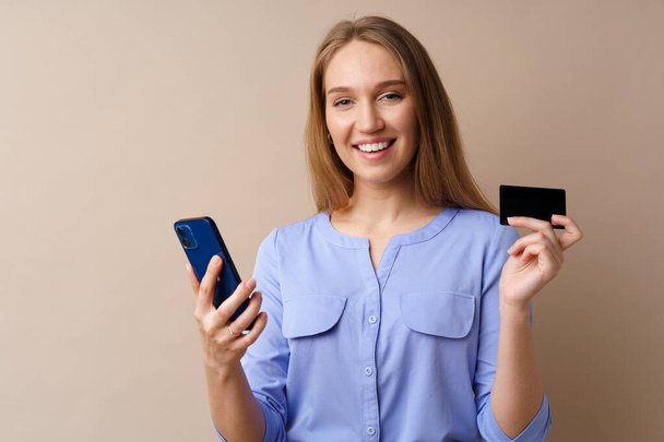 Happy young woman holding smartphone and credit card against beige background - Fotografie, Obrázek