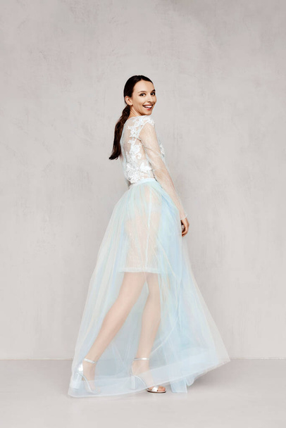 Beautiful young woman plays with hem of transparent pale tulle dresses with lace  - Fotó, kép