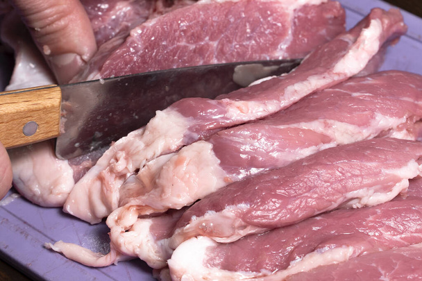 Schneiden Sie das Schweinefleisch oder Rindfleisch mit einem Messer in Nahaufnahme auf den Tisch. Zubereitung von Fleischgerichten und Lebensmitteln. Stücke von rotem Fleisch für Dönerspieß, Grill oder Döner.Rohes frisches Fleisch wird mit einem Messer geschnitten.Rezept - Foto, Bild