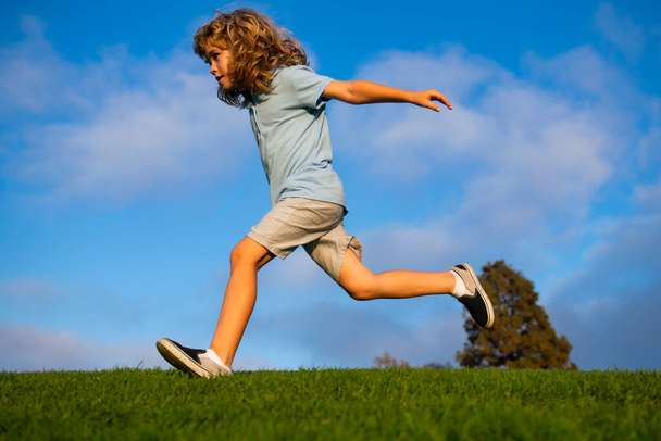 Child fun run outdoors. Kid playing in summer park. Little boy running on green fresh grass field. - Foto, imagen
