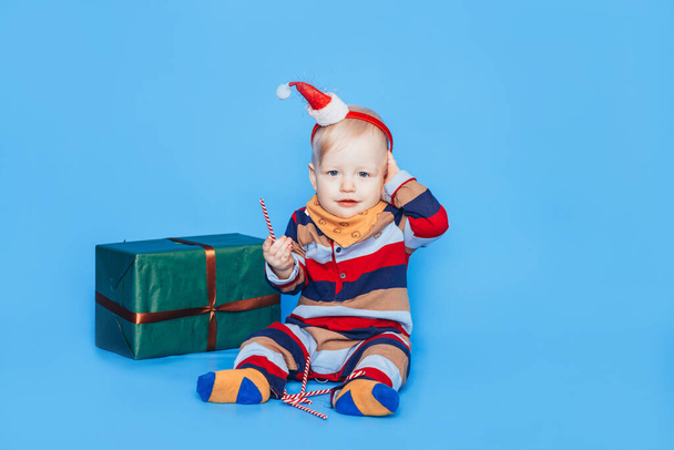 Μικρό αγόρι με καραμέλα και δώρο μπροστά από το μπλε φόντο. - Φωτογραφία, εικόνα