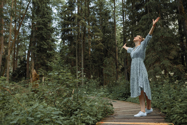 Νεαρή όμορφη γυναίκα αναπνέει καθαρό αέρα στο δάσος σηκώνοντας τα χέρια της ψηλά. Έννοια των υπαίθριων δραστηριοτήτων. αντίγραφο χώρου. - Φωτογραφία, εικόνα
