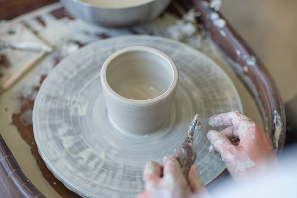 Female Potter creëert een aarden pot op een pottenbakkerswiel - Foto, afbeelding