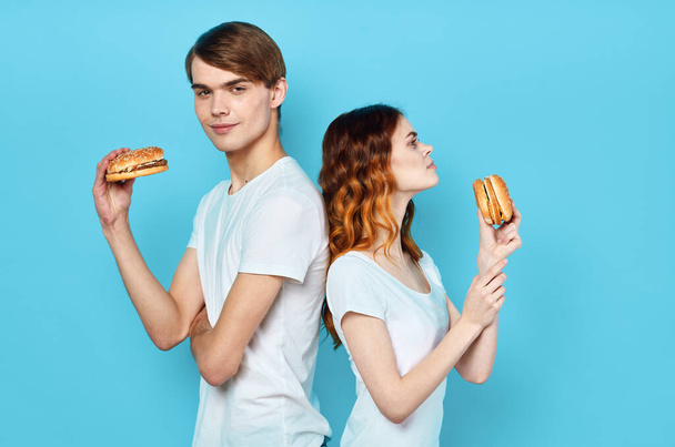 nuori pari valkoisissa t-paidoissa hampurilaiset käsissään pikaruokaa välipala - Valokuva, kuva