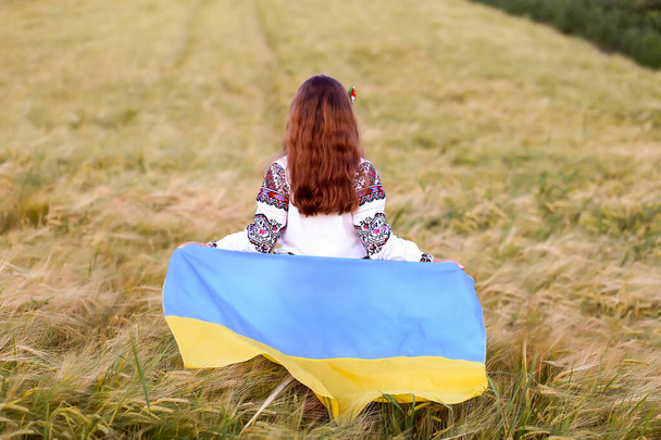Pitkätukkainen ukrainalainen tyttö kansallispuvussa ja vyshyvanka kävelee keltasinisellä lipulla heiluttavan spikelettikentän poikki. Ukrainan itsenäisyyspäivä, perustuslakipäivä, Vishivanka-päivä - Valokuva, kuva
