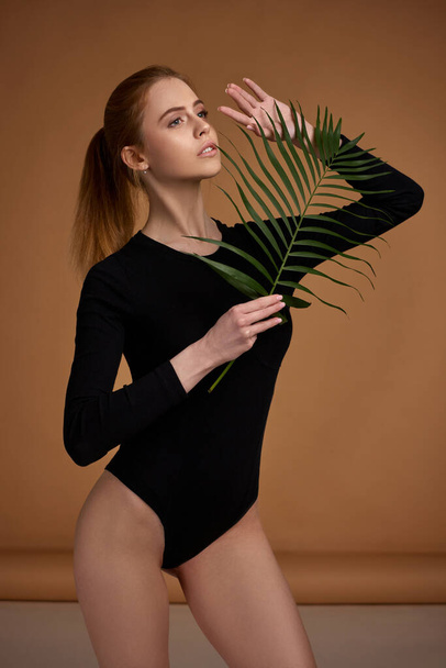 woman with perfect body in bodysuit holding palm leaves - Фото, изображение