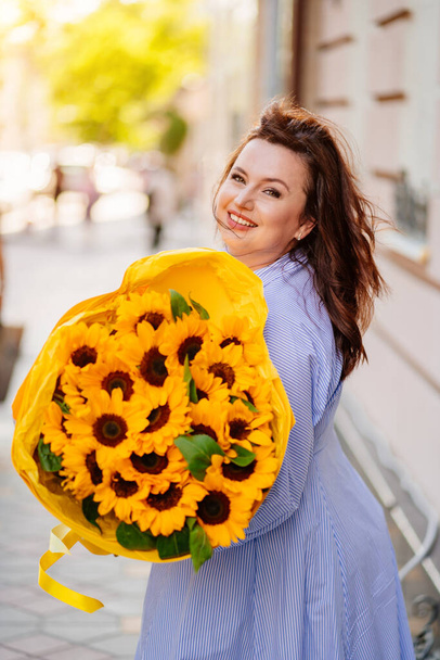 Onnellinen nainen valtava kukkakimppu koriste auringonkukat kävelee pitkin kaupungin katua - Valokuva, kuva