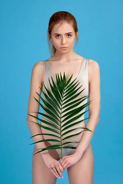 woman with perfect body in bodysuit holding palm leaves - Photo, image