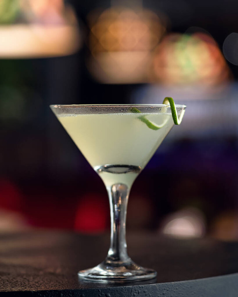 Bebida alcohólica. Vidrio Martini con decoración de cal sobre fondo oscuro, imagen abstracta borrosa. Copiar espacio - Foto, imagen
