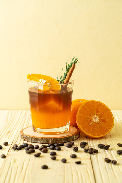 A glass of iced americano black coffee and layer of orange and lemon juice decorated with rosemary and cinnamon - Fotografie, Obrázek