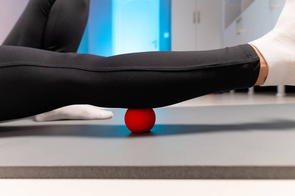 Close-up of self-massage of a sports woman indoors using a massage ball. Myofascial massage without a masseur. Elimination of pain in leg muscles - Foto, afbeelding
