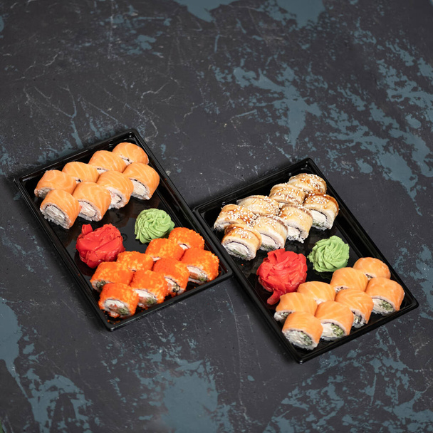 Comida para llevar. Dos juegos de rollos de sushi al revés en recipientes de plástico negro. Vista superior - Foto, Imagen
