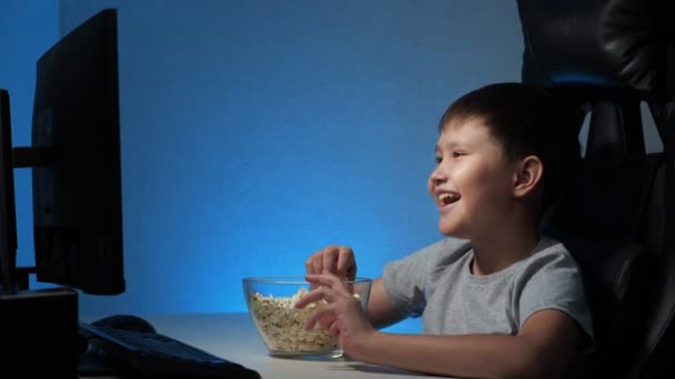 Chico mira el ordenador divertido video y come palomitas de maíz - Imágenes, Vídeo