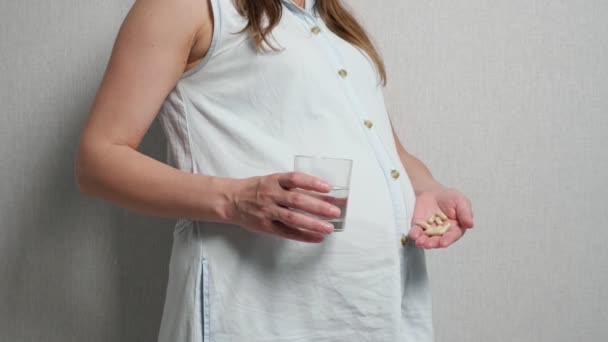 Неузнаваемая беременная женщина с лекарствами в одной руке и в другом стакане воды - Кадры, видео