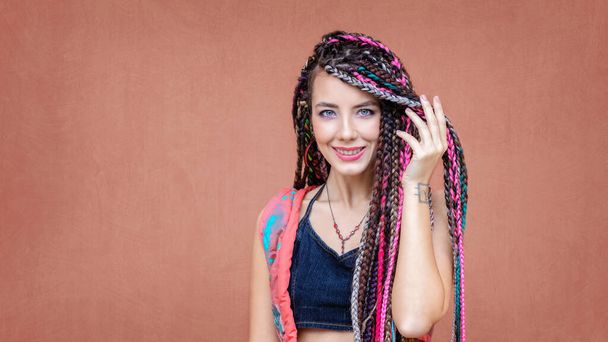 Boldog spanyol lány copfos és tetoválás mosolygós kamera szabadban színes háttér - Fotó, kép