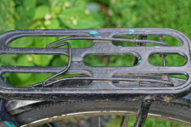Teil eines alten Retro-Fahrrads aus einem schwarzen Eisenstamm über einem Rad auf der Straße vor grünem Hintergrund - Foto, Bild