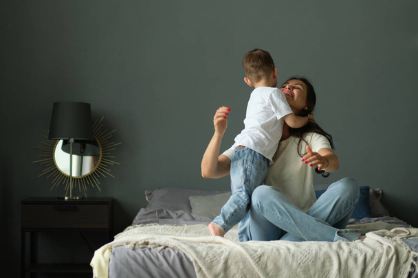 Matka przytula się ze swoim małym synkiem na łóżku. Rodzinne chwile, troska o dzieci. Koncepcja macierzyństwa, urlopu macierzyńskiego - Zdjęcie, obraz