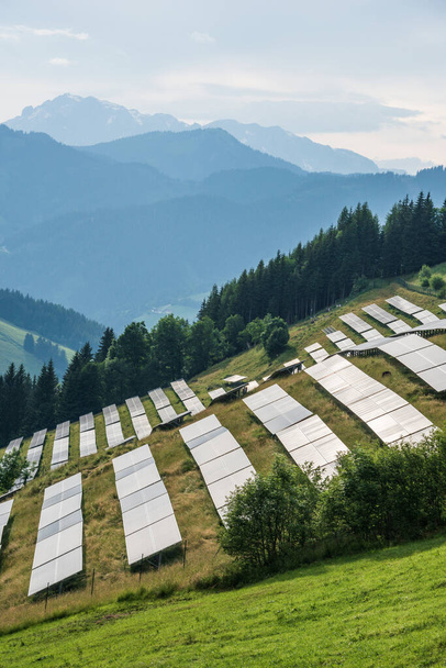 Сонячна електростанція, фотогальванічна ферма, розташована на гірському схилі Альп. Зелена пасовищна трава і блакитне небо і гори створюють свіжий і екологічний образ.. - Фото, зображення