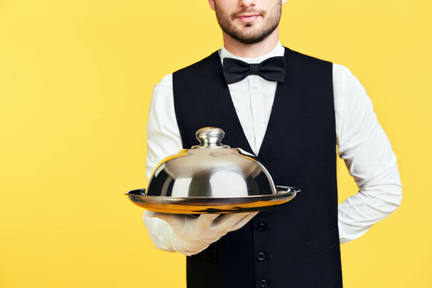 Young handsome waiter holding metal tray with cover ready to serve - Фото, изображение
