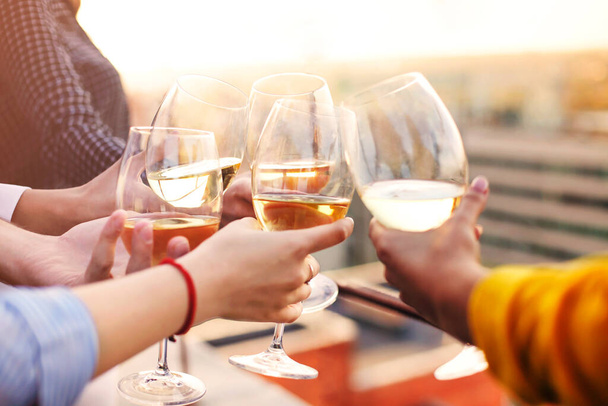 Groep anonieme mensen die wijnglazen klappen en toast uitbrengen tijdens een feestje op het dak - Foto, afbeelding