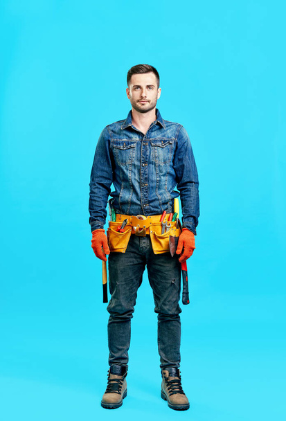 Full length portrait of handsome young male construction worker staying over blue background - Foto, Bild