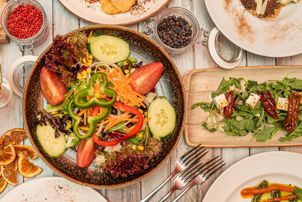 Nahoře obrázek zeleninového salátu a syrové čerstvé zeleniny, rukolový salát se sýrem Feta a sušenými rajčaty, vidličkami, červeným pepřem, černým pepřem, oranžovým suchým - Fotografie, Obrázek