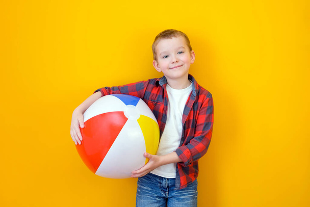 Summer vacation concept, portrait of happy cute little child, boy smiling and holding beach ball, child having fun with inflatable ball, studio shot isolated on yellow background - Фото, зображення
