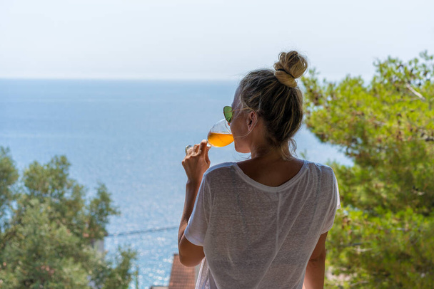 Mujer guapa en camisa blanca bebiendo Aperol Spritz y disfrutando de la vista del mar abierto - Foto, Imagen