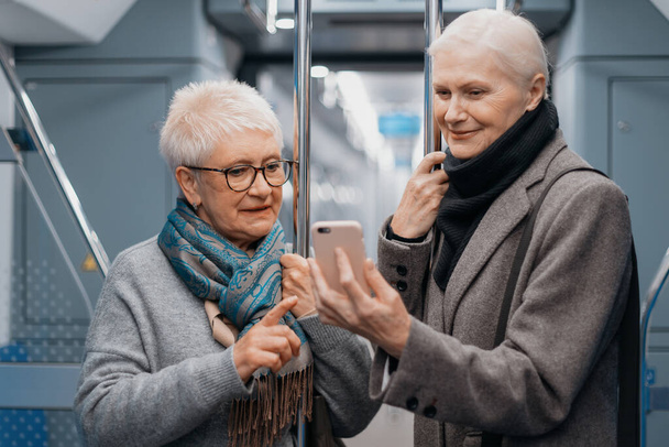 two mature women using a smartphone in a subway car. - Photo, Image