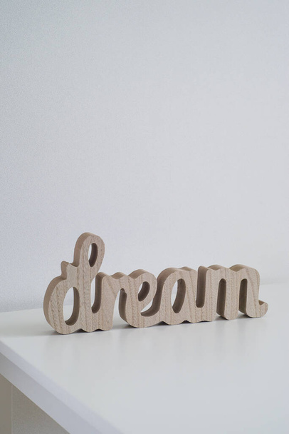 against the background of a white wall corner of a white table. on the table in the center of the frame wooden inscription dream diagonally figurine brown word decor . place for text. childrens room - Foto, Bild