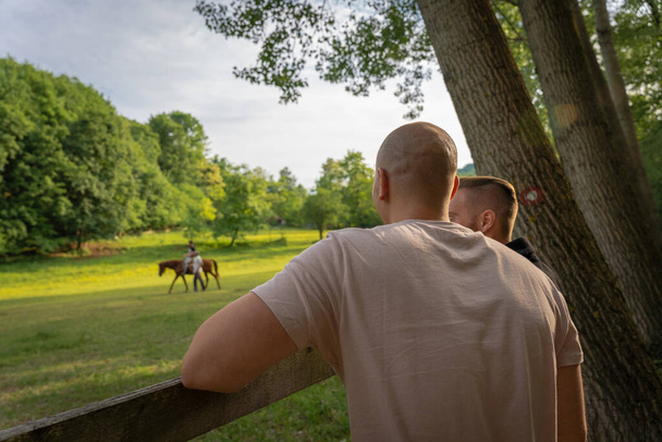 Δυο μυώδεις άντρες μιλάνε και βλέπουν μια βόλτα με άλογο. - Φωτογραφία, εικόνα