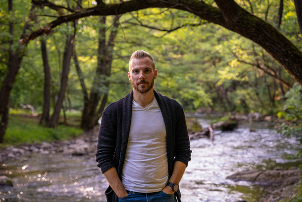 Молодой модный парень позирует для фото в природе с рекой на заднем плане - Фото, изображение