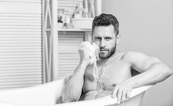 man wash muscular body with foam sponge. hygiene and health. Sexuality and relaxation. desire and temptation. personal care. Sexy man in bathroom. Macho sitting naked in bathtub washing with sponge - Photo, image