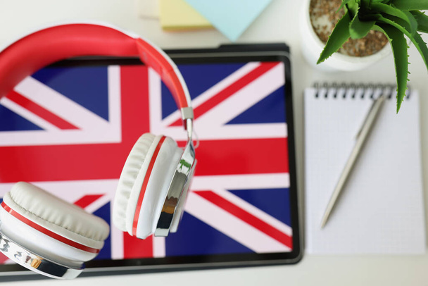 Tablet with image of British flag with headphones and notebook with pen lie on table - Foto, imagen