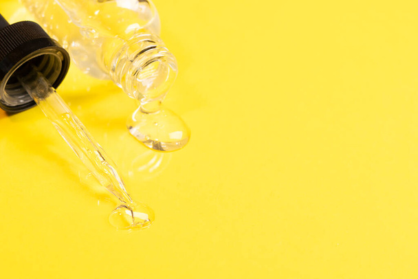 Kosmetische Flüssigkeit Gel Serum Schmiermittel fließt aus der Glasflasche Tropfer gelben Hintergrund. Gesichts- und Körperpflege - Foto, Bild
